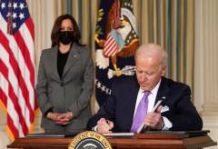 President Joe Biden signs papers with Vice President Kamala Harris in the background